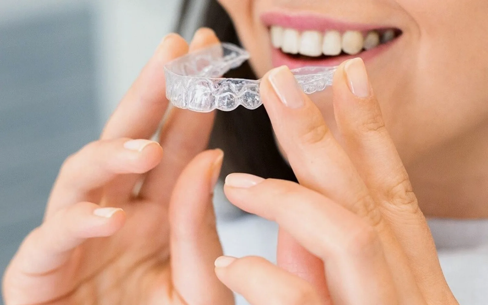 Adult holding a clear orthodontic aligner near the teeth